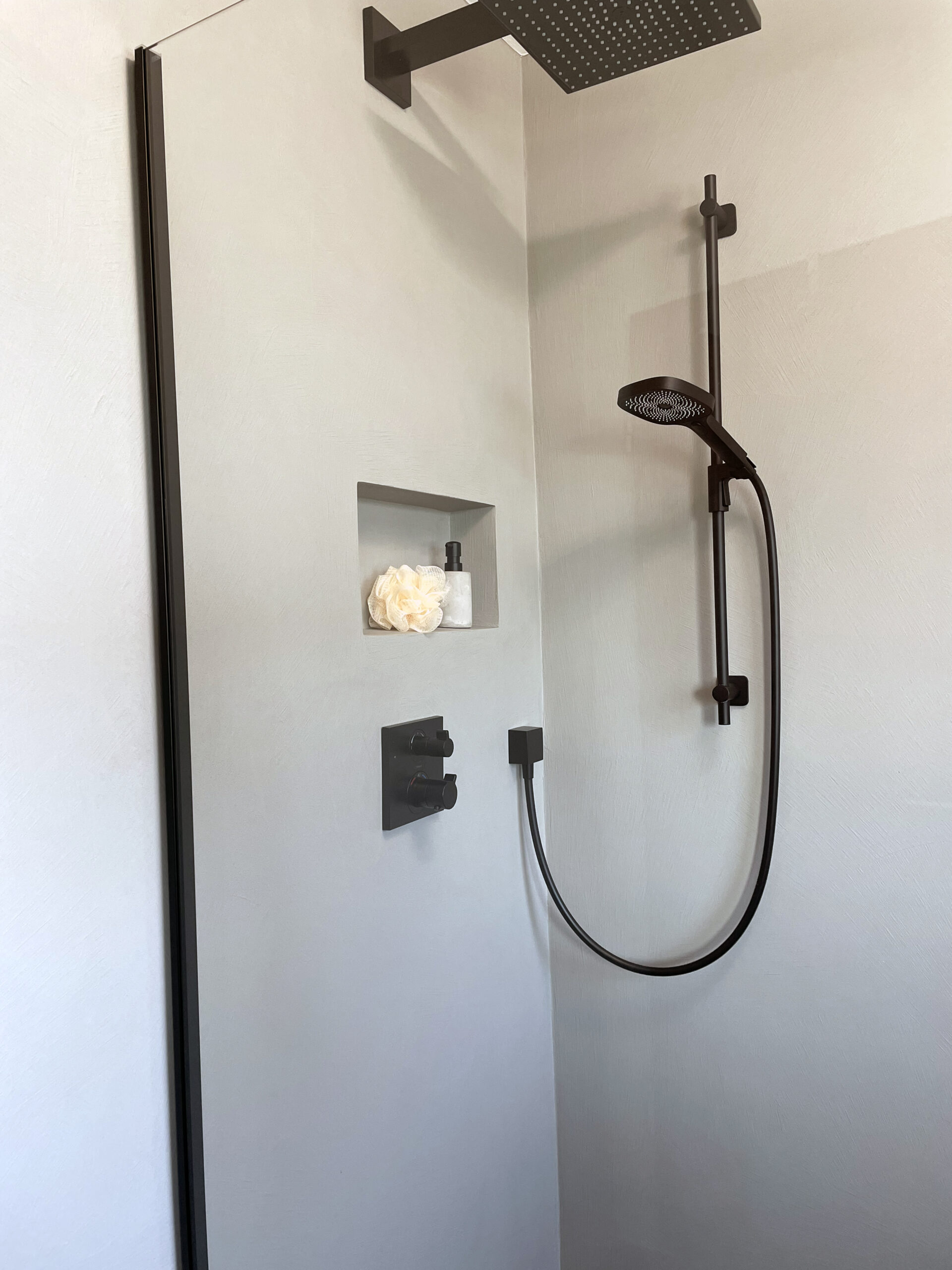 Schwarze Regendusche und Handbrause vor heller fugenloser Wand