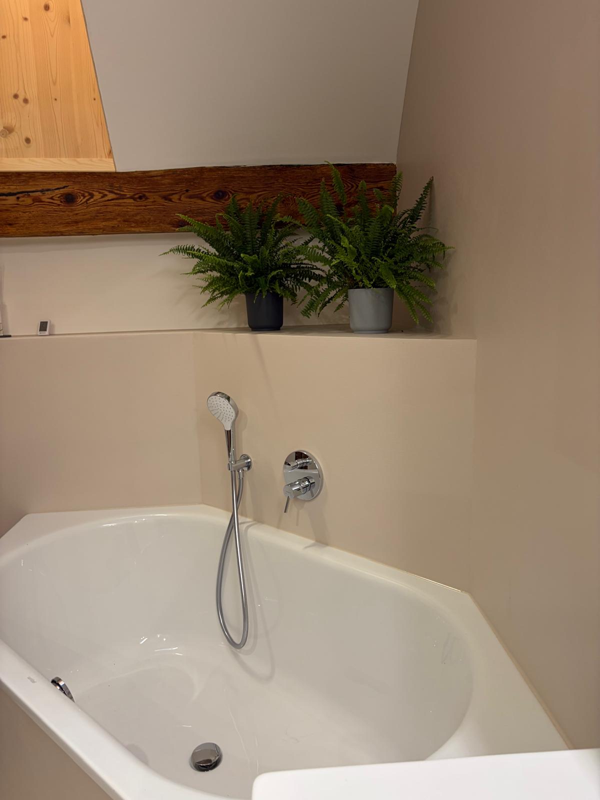 Badewanne vor fugenloser Wandfläche und historischem Holzbalken in Hailfingen